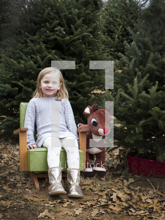 girl toddler in a chair in a Christmas tree lot 