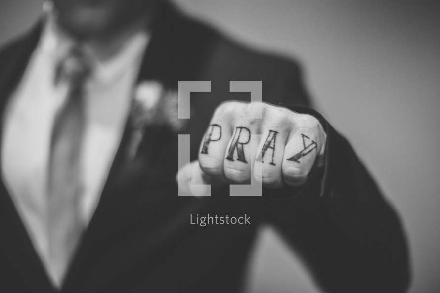 "Pray" written on the knuckles of a man in a suit.