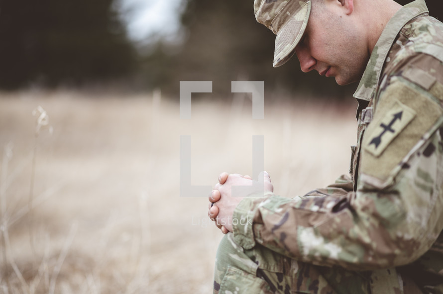 serviceman kneeling in prayer in a field 