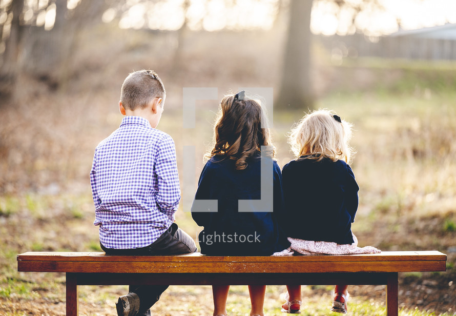 siblings sitting on a bench with backs to the camera 