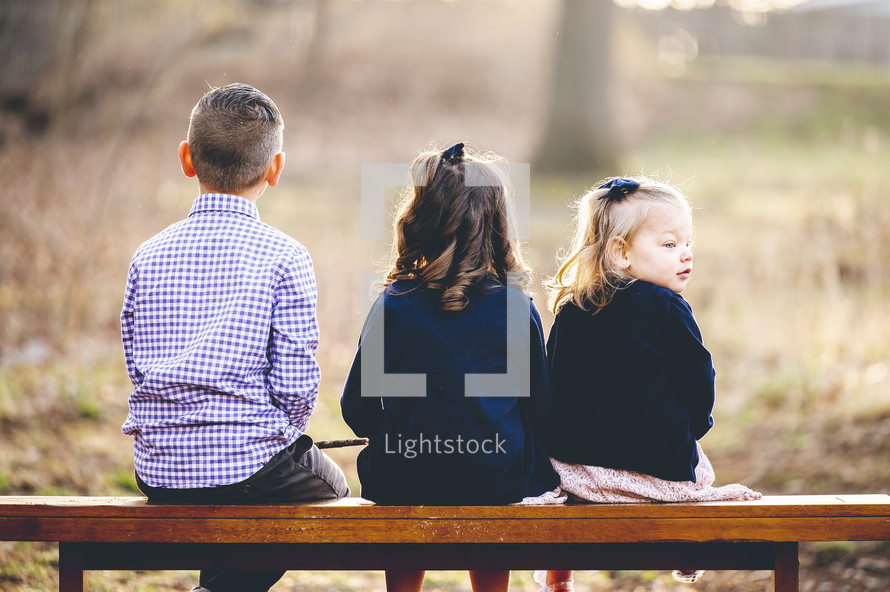 kids sitting on a bench with backs to the camera 