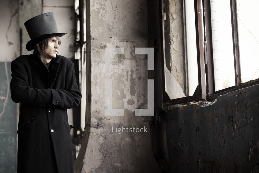 man in a vintage black trench coat and top hat in an abandoned building 