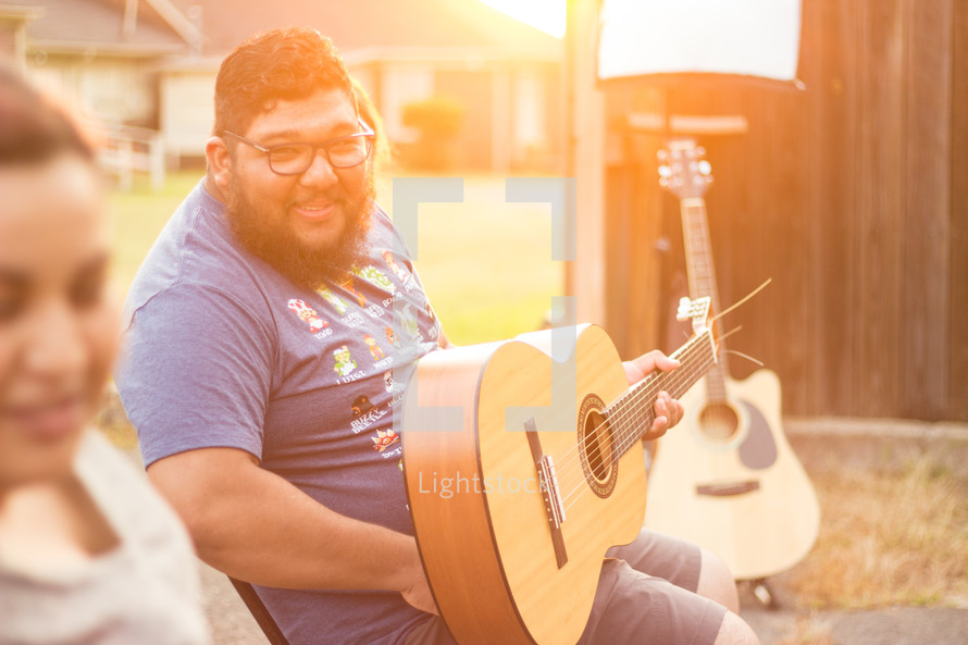 man sitting in a chair outdoors holding a guitar 