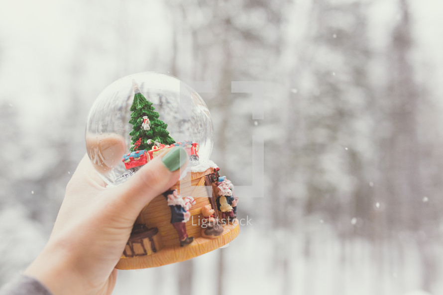 a woman holding a snow globe outdoors in falling snow 