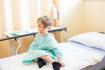 a boy child in a hospital gown on a stretcher 