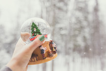 a woman holding a snow globe outdoors in falling snow 