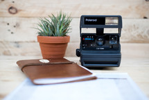 journal, Polaroid Camera, and houseplant on a desk 