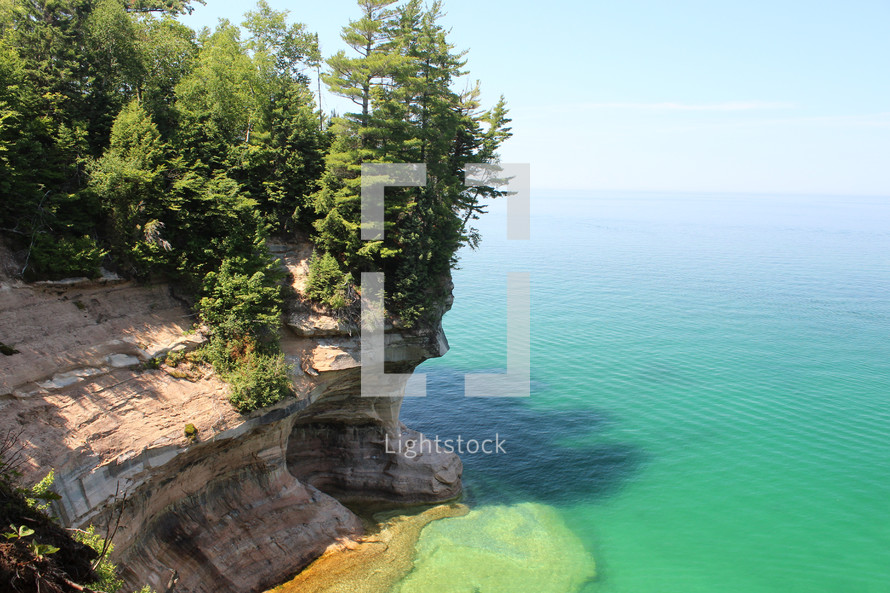 trees at the top of a steep rock cliff along a shore 