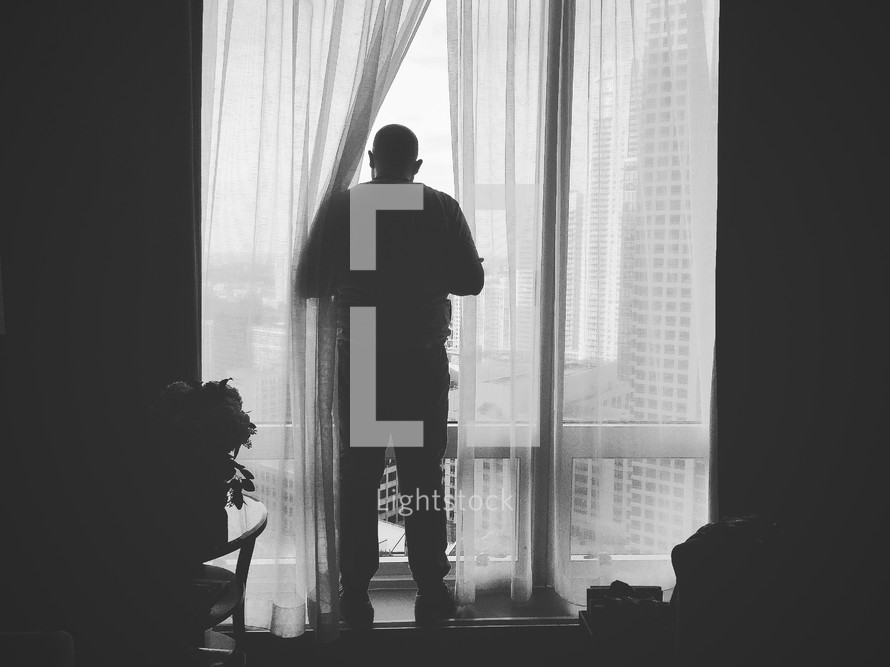 man looking out a hotel bedroom window 