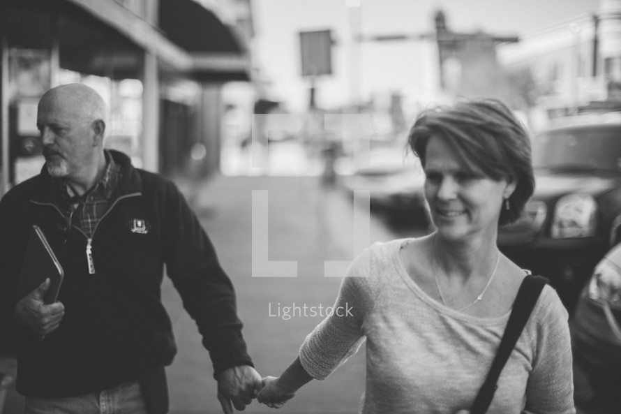a couple holding hands walking down a sidewalk 