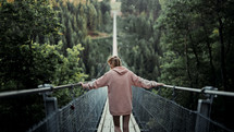 a woman crossing a swinging bridge 