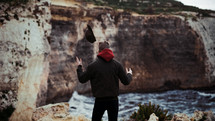 man standing on a rugged shore with arms raised 