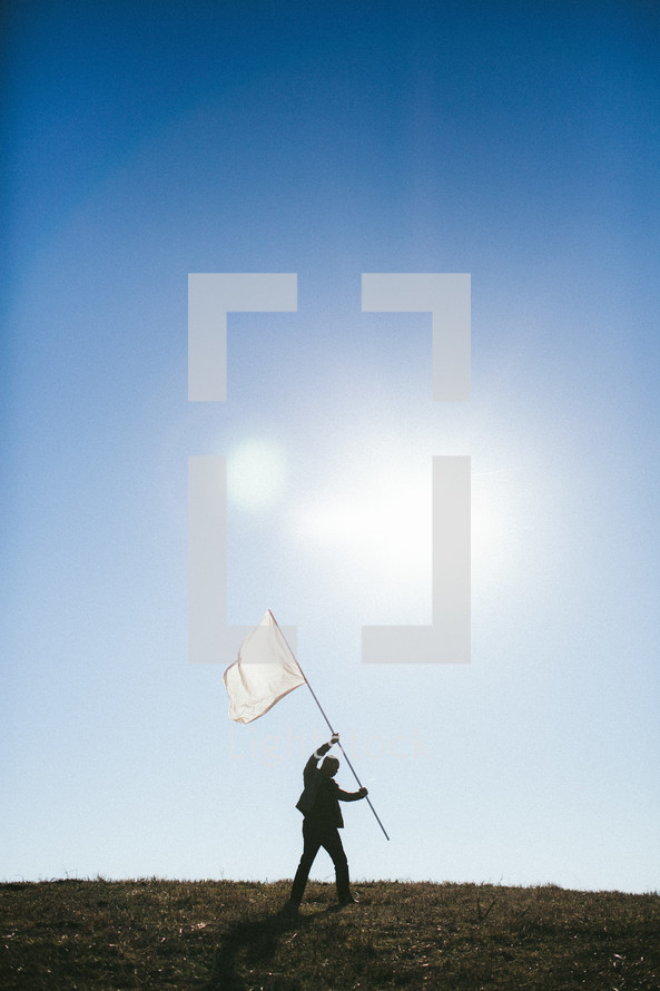 Silhouette of man on hill carrying white flag.