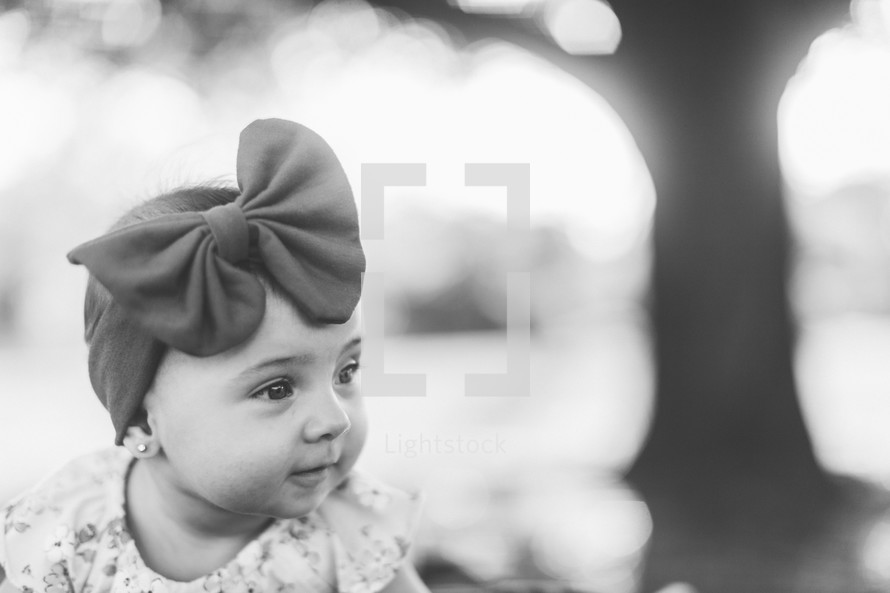 an infant girl in a headband with a bow outdoors 
