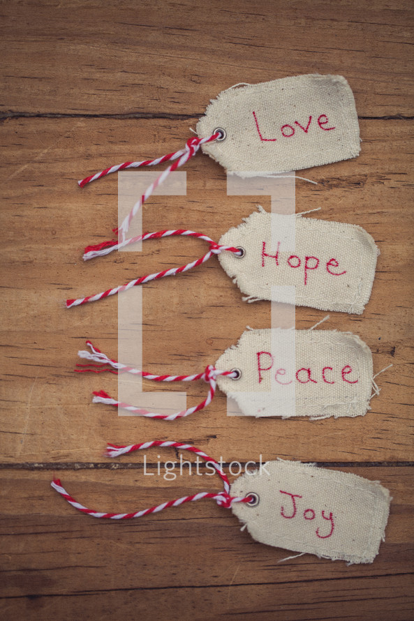 Christmas gift tags, labeled Love, Hope, Peace, and Joy, on a wooden table.