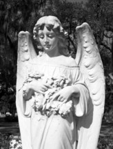 A tall and ornate statue of an angelic female figure stands in a historic cemetery in the southern United States of America where many historic figures are buried and serves as a historic landmark. 