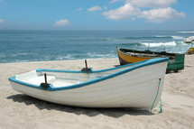 Two boats on a sandy beach near the ocean shore.