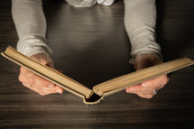 Hands holding a book on a dark wood table