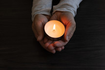 Hands holding single candle on a dark wood table