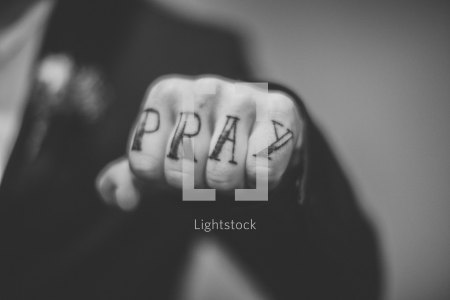 "Pray" written on the knuckles of a man's hand.