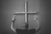 Man facing cross on the wall with arms raised.