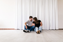 a couple snuggling sitting on the floor of an empty house 