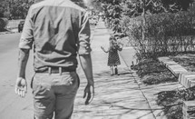 father and daughter walking down a sidewalk 
