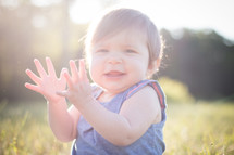 toddler girl sitting in bright sunlight clapping hands 