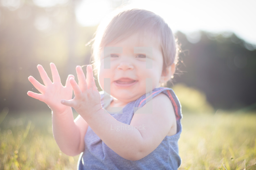 toddler girl sitting in bright sunlight clapping hands 