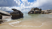 Large boulders on sandy beach with cloudscape behind 