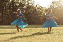 Two young women in blue dresses dancing in a field.