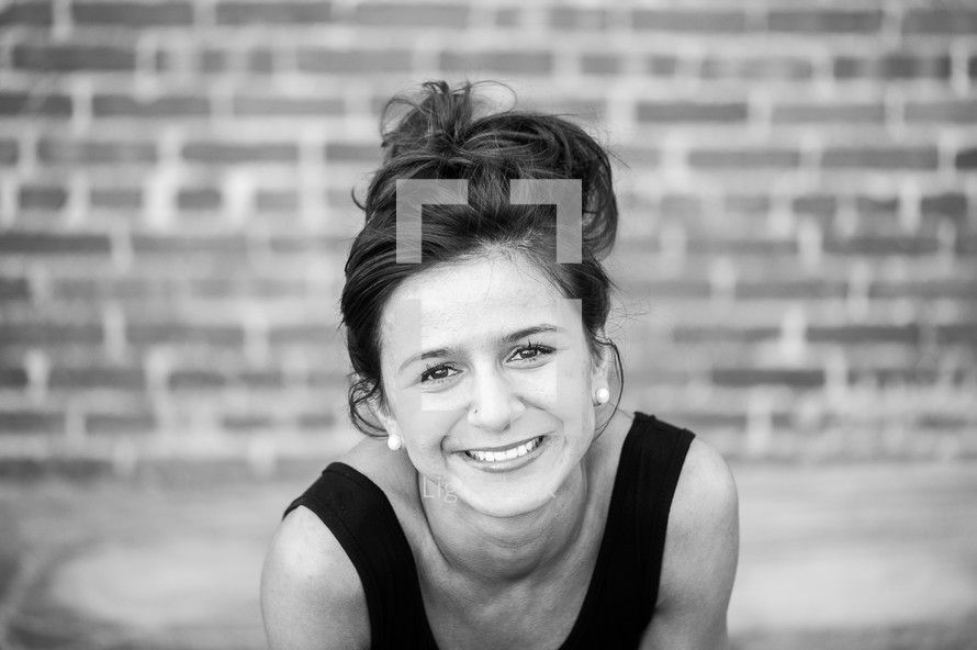 Smiling woman sitting in front of a brick wall.