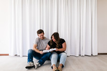 a couple sitting on the floor reading a Bible together 