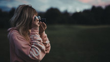 a woman taking a picture with a camera at sunset 