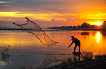 A man casting a net at sunset 