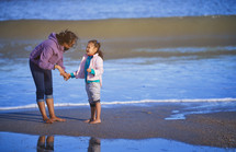 mother and daughter walking barefoot on a beach 