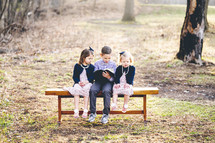 siblings sitting on a bench outdoors reading a Bible together 