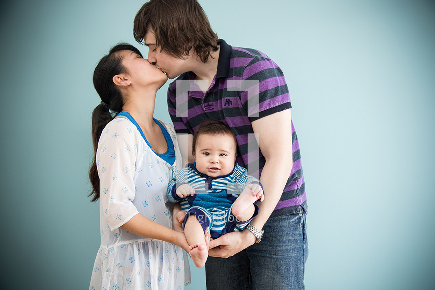 Kissing couple cradling their infant child.