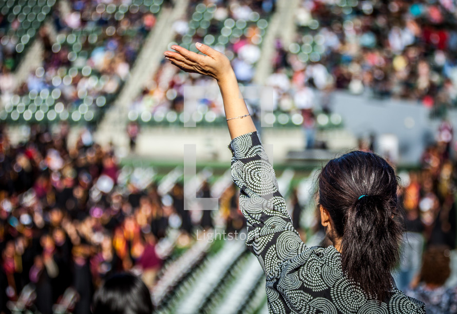 a woman in the audience with a raised hand at a graduation ceremony.