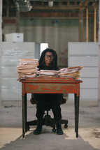 an overworked woman standing behind a desk covered in files 