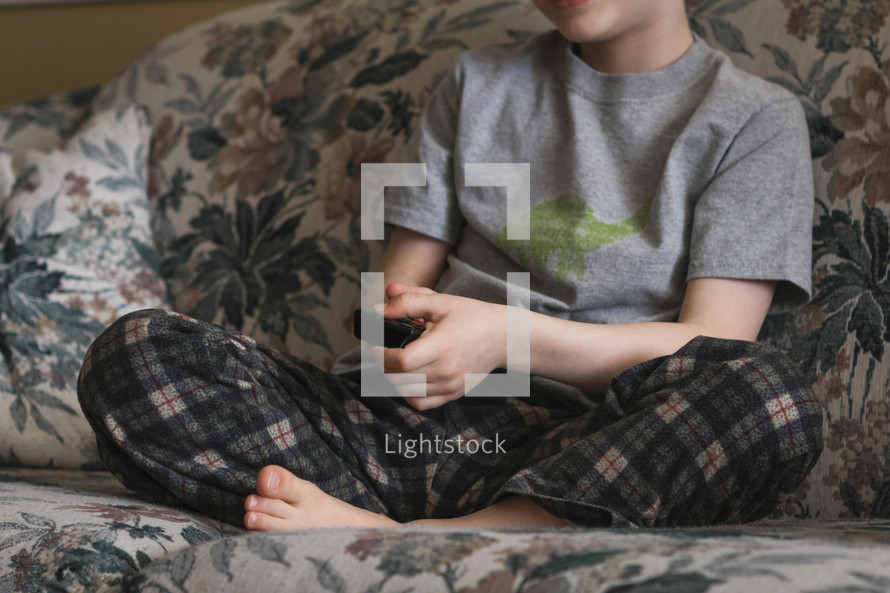 boy sitting on a couch with a remote control 