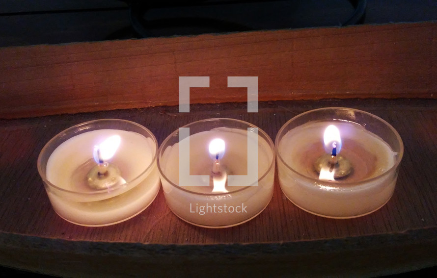 Three wax candles burning together during a candlelight worship service during Christmas Eve or some other occasion at church. 