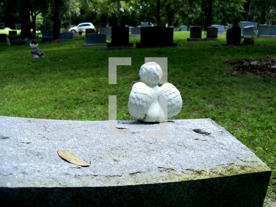 A white Cherub Angel sits and watches over a grave and surveys all that is in its view around him as though it were watching over the graves of the departed in his watch and territory. 