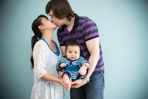 Kissing couple cradling their infant child.