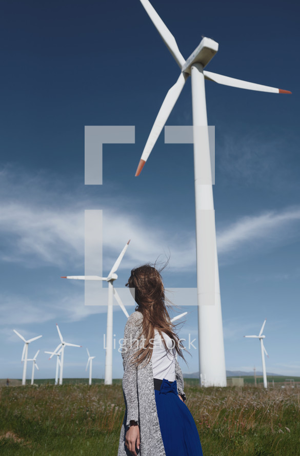 a woman standing under wind turbines 