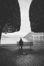 a woman sitting on a park bench looking out over water in fog 