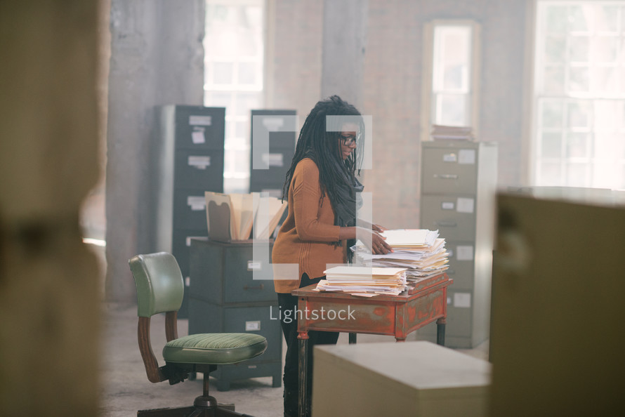 overworked woman standing at a desk covered in files 
