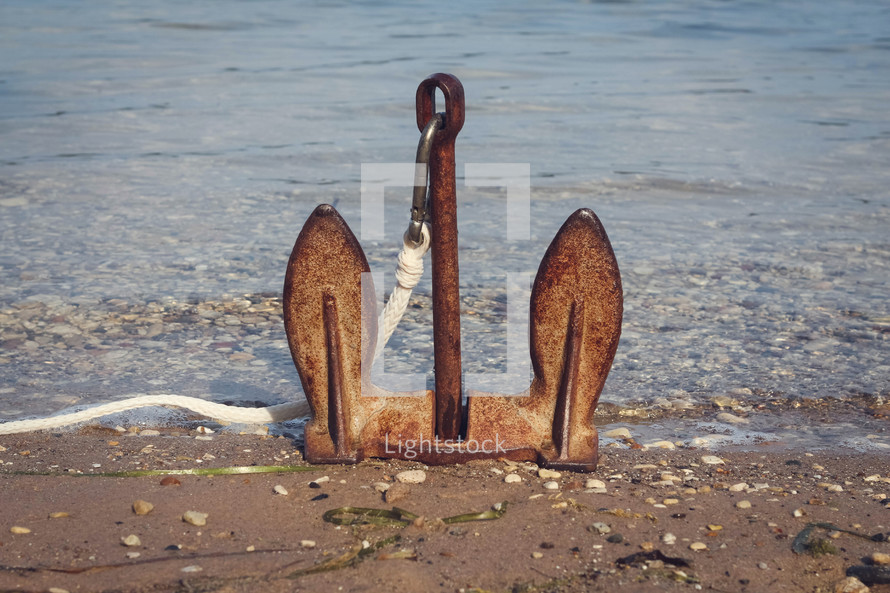rusty anchor sitting upright on the shore