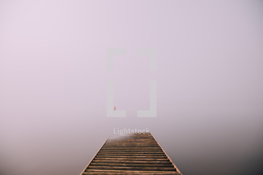 A pier on a fog covered lake.