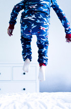 a boy in pajamas jumping on a bed 